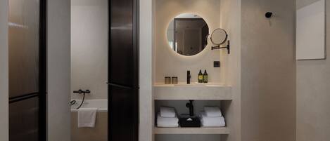 A modern bathroom with a bathtub, a round mirror, and shelves with towels and toiletries.