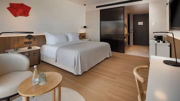 Una habitación de hotel moderna con cama, mesitas de noche, un escritorio, una silla, un televisor y una obra de arte abstracta roja en la pared.
