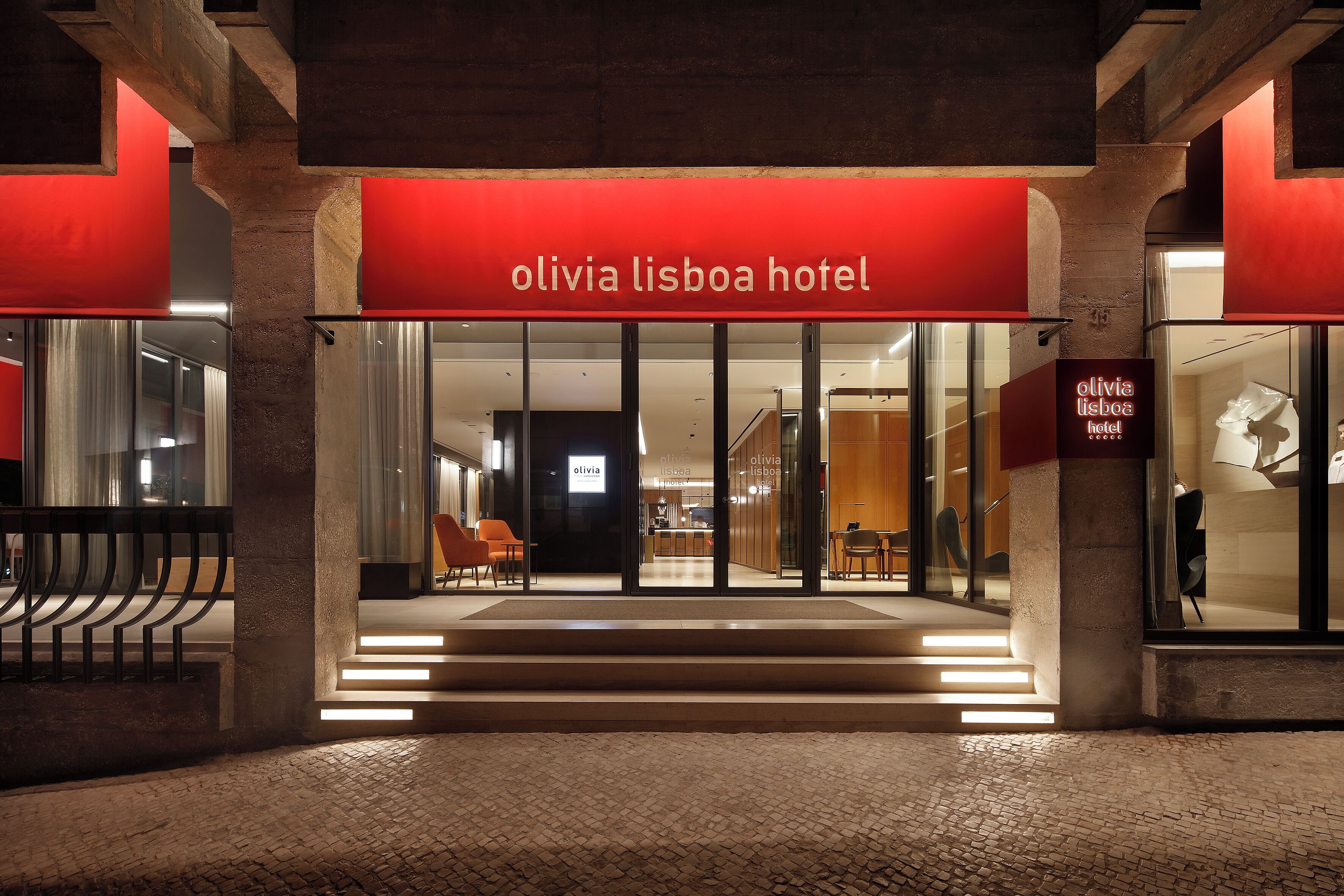 The entrance of the Olivia Lisboa Hotel with a red awning, glass doors, and a staircase leading to the entrance.