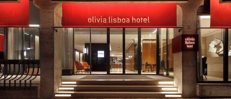 The entrance of the Olivia Lisboa Hotel with a red awning, glass doors, and a staircase leading to the entrance.