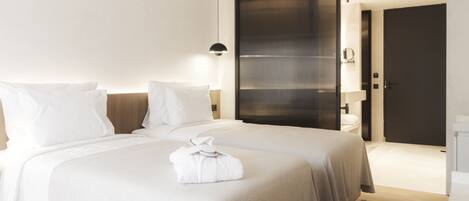 A modern hotel room with two beds, a large sliding door, a bedside table, and a hanging light fixture.