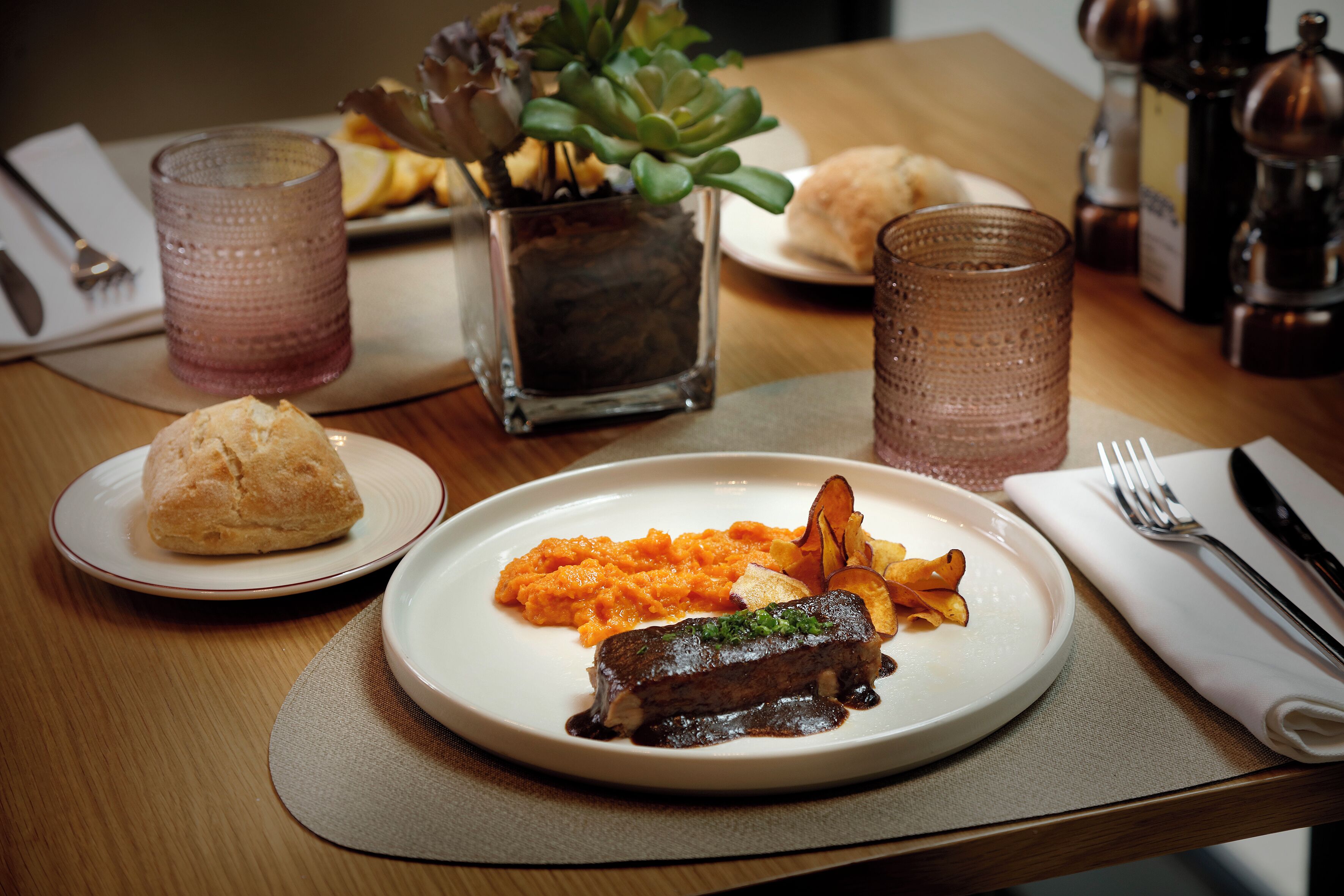 A dining table with a plate of food, a glass, a napkin, and a fork.