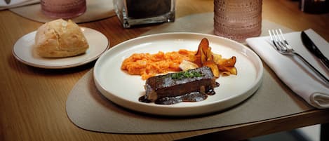 A dining table with a plate of food, a glass, a napkin, and a fork.