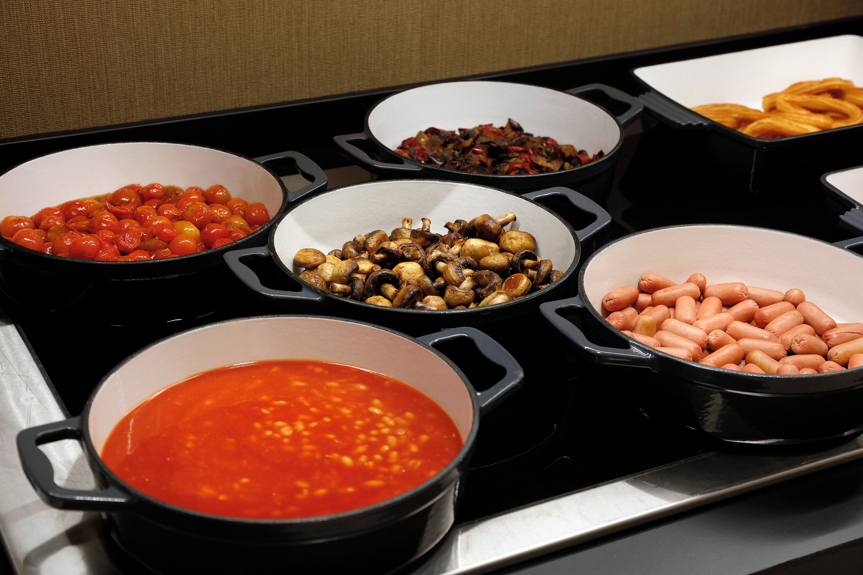 Ein Buffet mit verschiedenen Speisen, darunter Tomaten, Pilze, Würstchen und rote Soße.