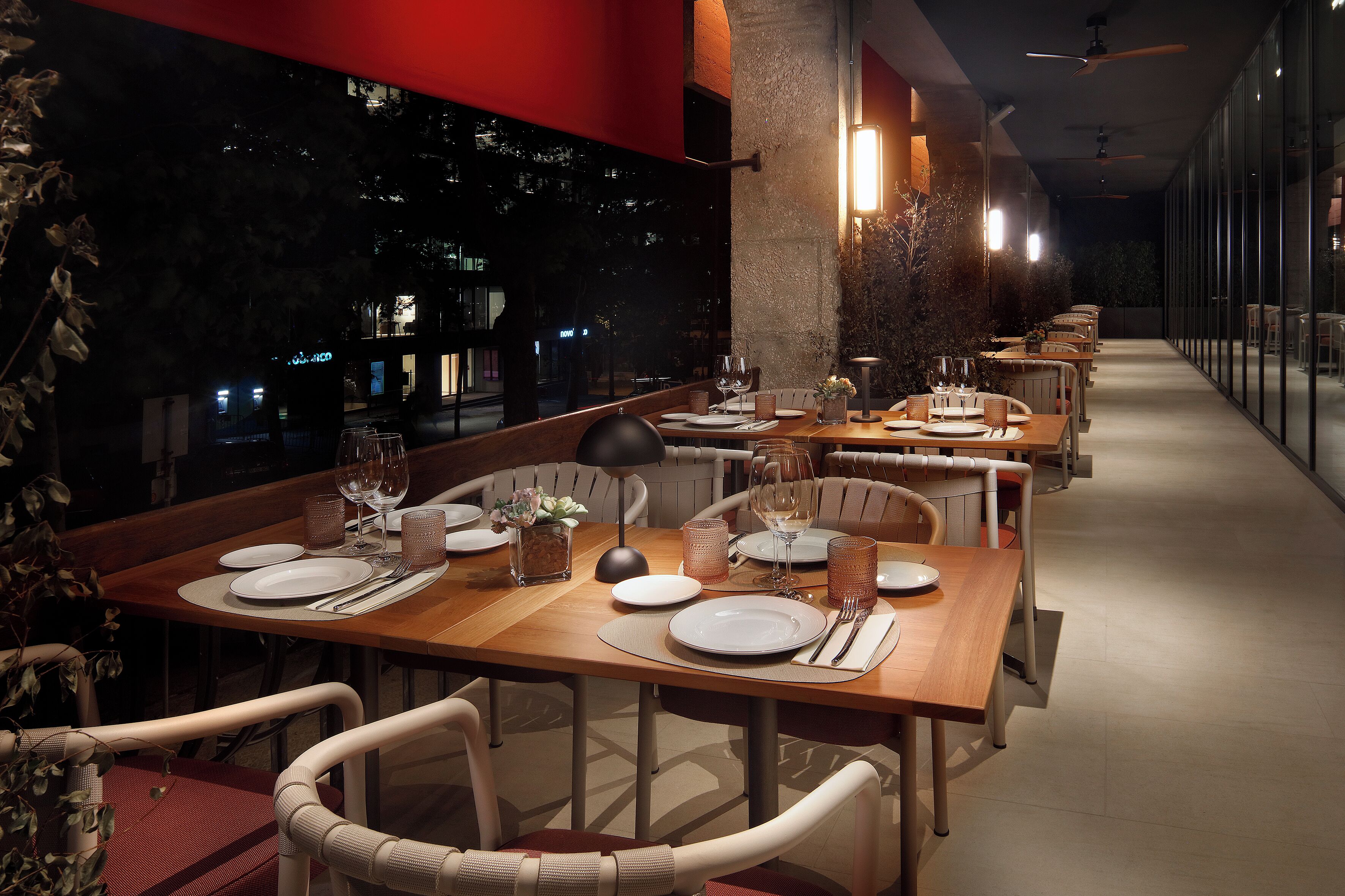 Een restaurant met meerdere tafels, stoelen en uitzicht op de stad in de avond.