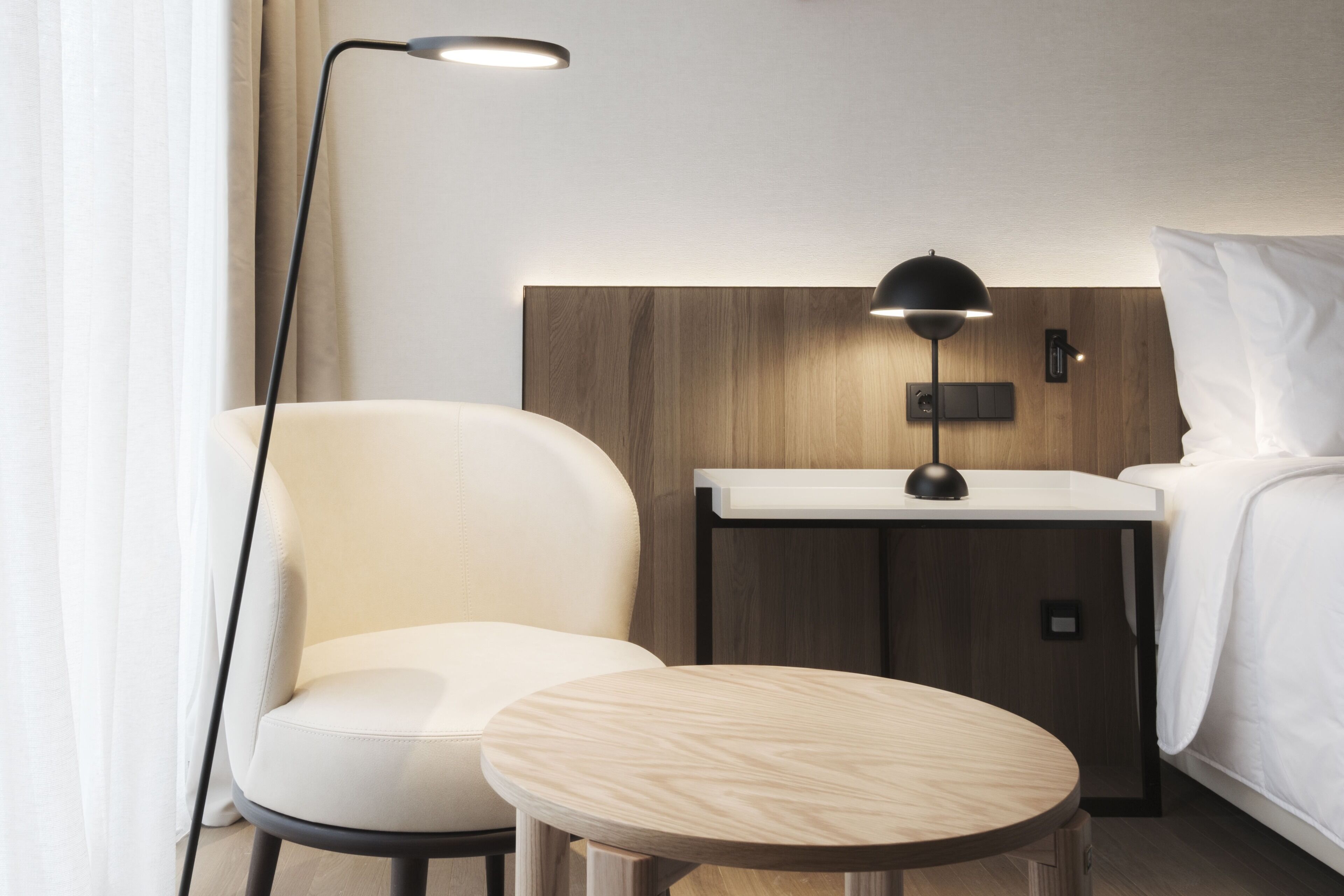 Een moderne hotelkamer met een houten hoofdeinde, een nachtkastje, een lamp, een stoel en een bed.