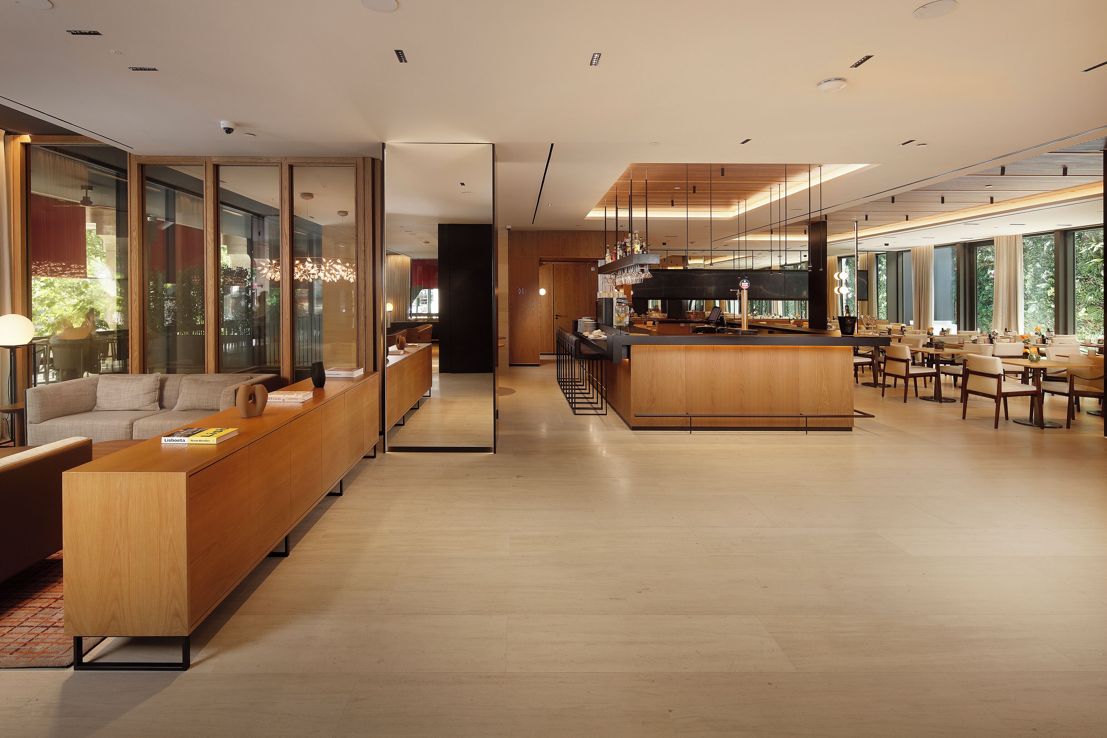 Een moderne hotellobby met een lange receptiebalie, een zithoek met banken, een bar en grote ramen met uitzicht op het omliggende landschap.