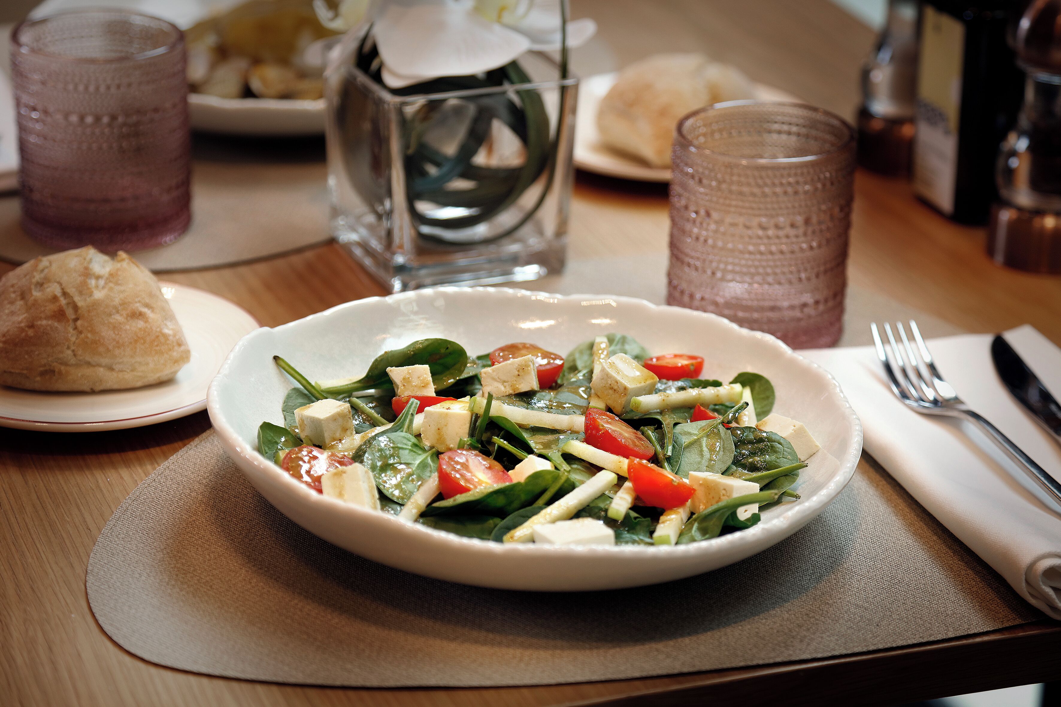 A plate of salad with croutons and cheese, a glass of beverage, and a napkin with a fork on a table.