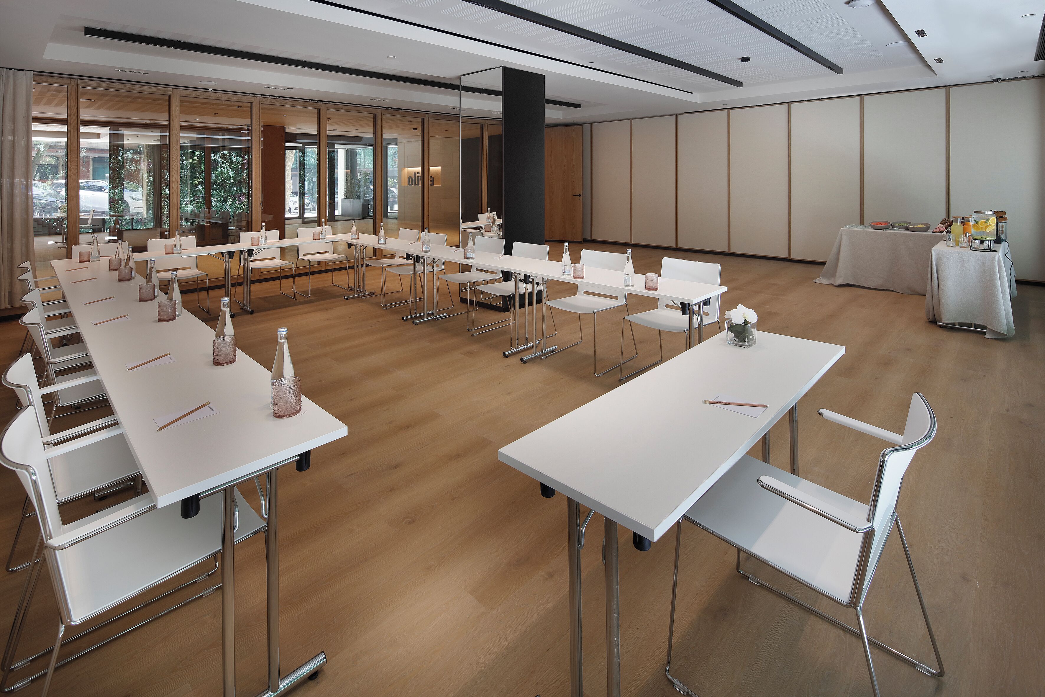 A conference room with white tables and chairs, large windows, and a high ceiling.