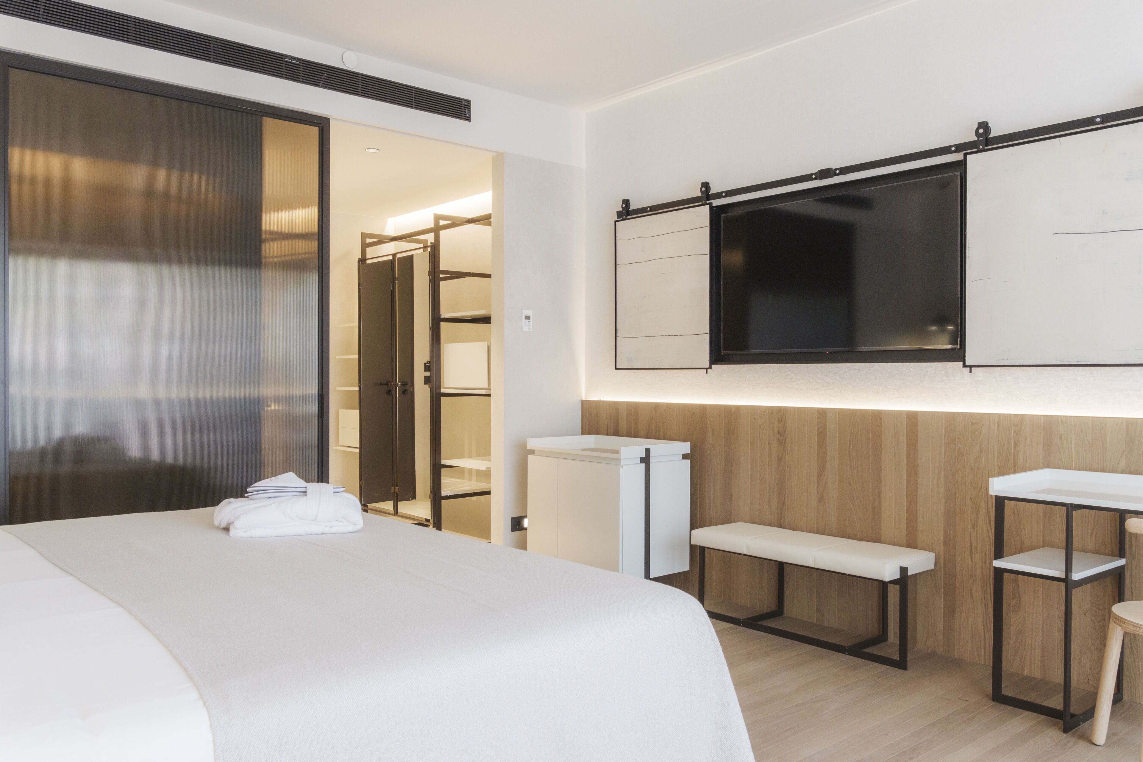 A hotel room with a bed, a bench, a small table, a TV, and a wardrobe.