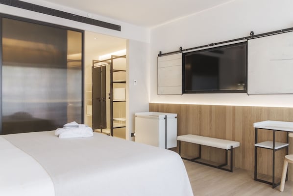 Une chambre d’hôtel avec un lit, une banquette, une petite table, un téléviseur et une armoire.