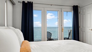A bedroom with a large bed, a view of the sea through a glass door, and a chair by the door. - Amazing Water views! Ocean front, HotTub & More! (Plymouth)