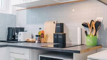 Une cuisine équipée d’une machine à café, de boîtes à thé et à sucre, d’une planche à découper et d’un porte-ustensiles.