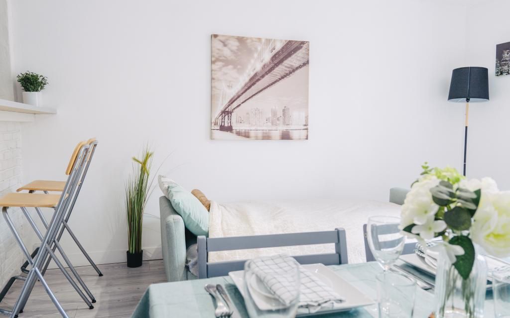 Une pièce minimaliste comprenant un lit, une table dressée pour le repas, une chaise, une lampe et un tableau accroché au mur.
