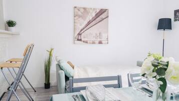 Une pièce minimaliste comprenant un lit, une table dressée pour le repas, une chaise, une lampe et un tableau accroché au mur.
