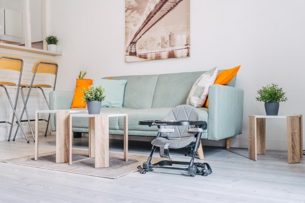 Een moderne woonkamer met een groene bank, een kinderwagen en een stadsgezichtschilderij aan de muur.