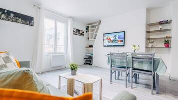 Un salon moderne avec un canapé, une table à manger et des chaises, un téléviseur et une vue sur la ville.