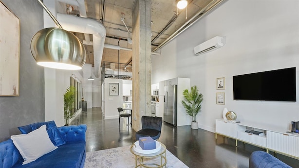 A modern living room with a blue sofa, a round gold table, and a flat-screen TV mounted on the wall. - Stylish Loft Deep Ellum Dallas Tx (Dallas)