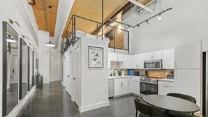 A modern kitchen with white cabinets, a microwave, oven, and a dining area with a table and chairs. - Stylish Loft Deep Ellum Dallas Tx (Dallas)