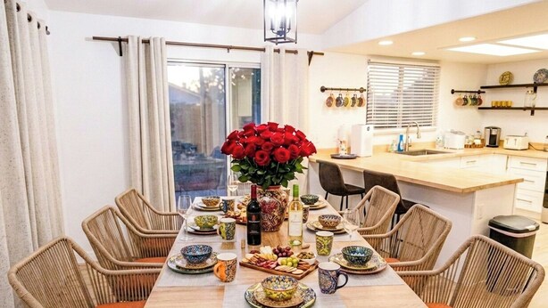 A dining area with a wooden table, wicker chairs, and a vase of red roses. - Near ​JT Park: Hot Tub, Cinema, Arcade Game, GameRM  (Yucca Valley)