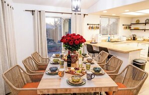 A dining area with a wooden table, wicker chairs, and a vase of red roses.