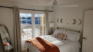 A bedroom with a bed, a nightstand, a lamp, a ceiling fan, and a view of the outdoors through a sliding door. - Near ​JT Park: Hot Tub, Cinema, Arcade Game, GameRM  (Yucca Valley)
