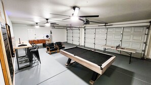 A pool table in a room with a ceiling fan, a foosball table, and a seating area.