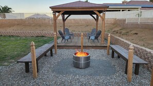 An outdoor patio with a fire pit, wooden benches, and two chairs. - Near ​JT Park: Hot Tub, Cinema, Arcade Game, GameRM  (Yucca Valley)