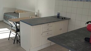 A compact kitchen with a small dining area, a bed, and a window providing natural light.