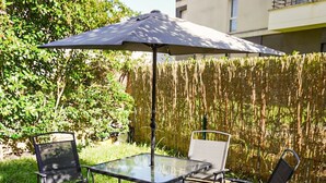 An outdoor patio with a glass table and four chairs, shaded by a large umbrella. - Apartment 5 min from Disney (Montévrain)