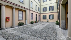 A courtyard with stone paving, buildings with multiple windows, and a few potted plants.