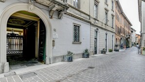 A street with a building entrance, a metal gate, and potted plants along the sidewalk.