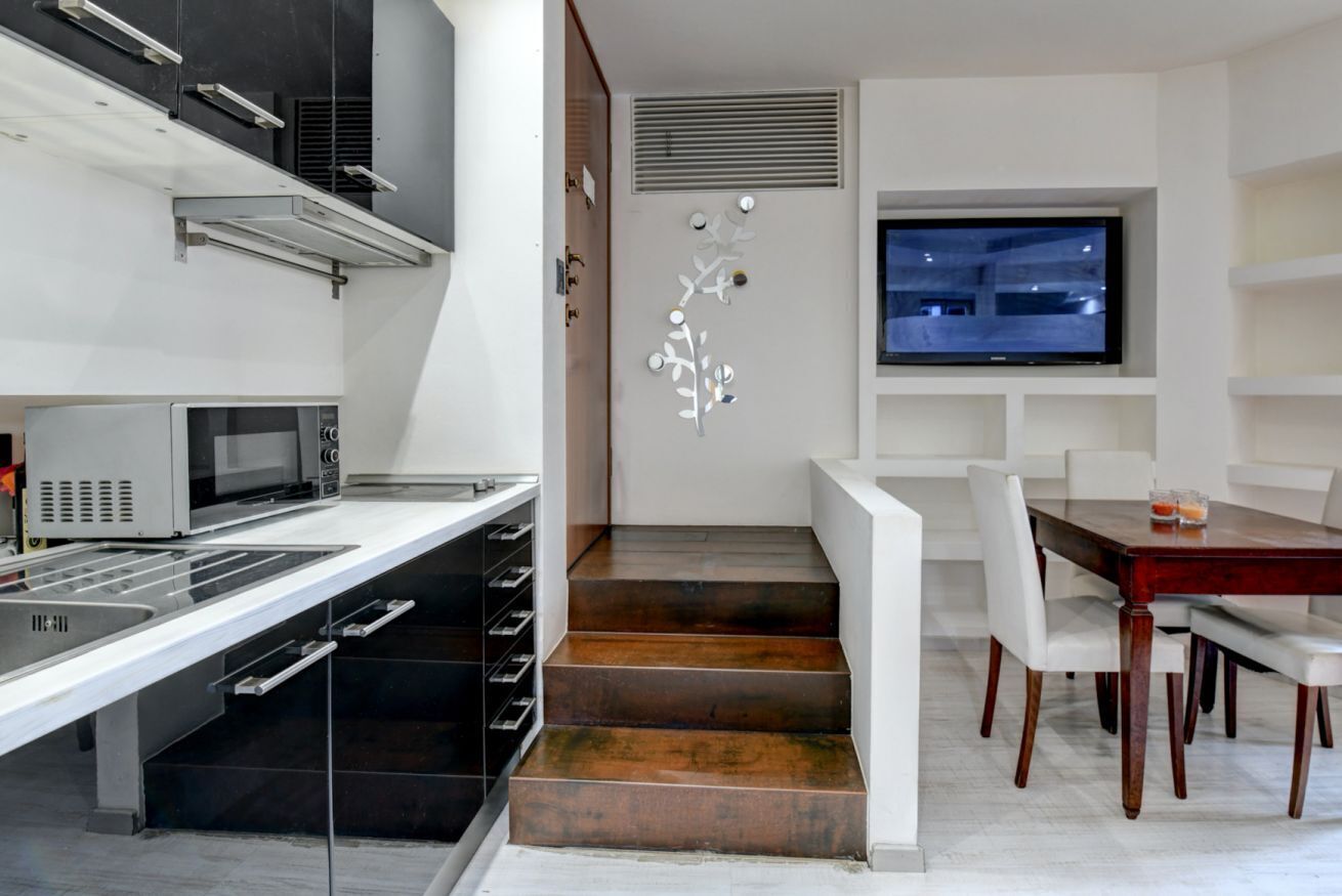 A modern kitchen with a microwave, a built-in oven, and a dining area with a wooden table and white chairs.