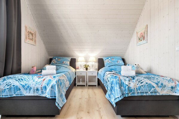 Een kamer met twee bedden, elk met een blauw beddegoed met patroon, een nachtkastje met lamp en een kleine tafel met een plant.