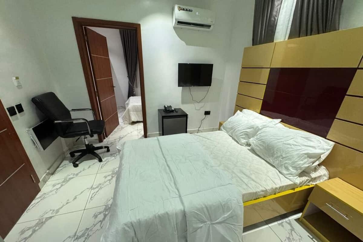 Een hotelkamer met een bed, een bureau, een stoel, een airconditioner, een televisie en een kledingkast.