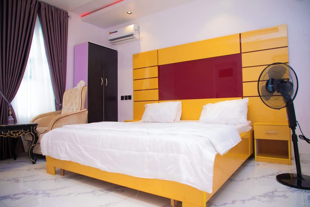 Een slaapkamer met een bed, een stoel, een kledingkast, een airconditioner en een ventilator.