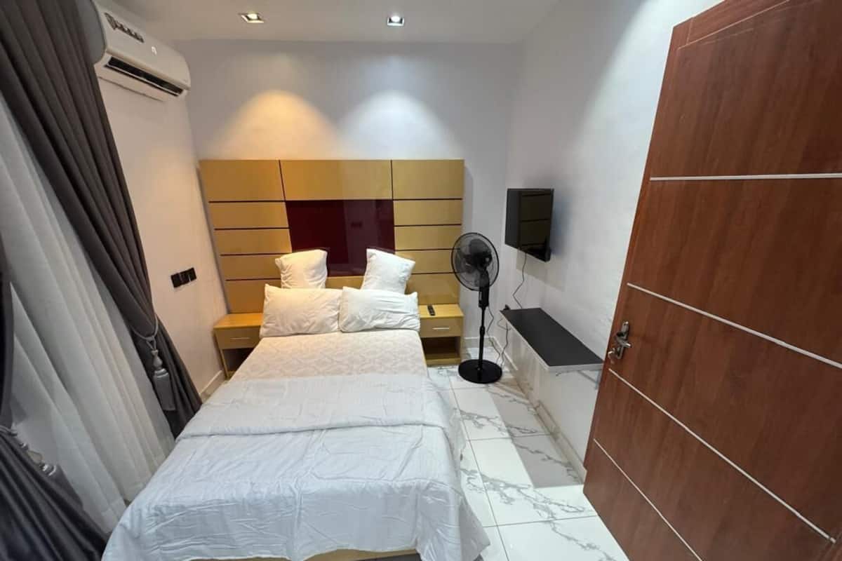 Een hotelkamer met een bed, een houten garderobe, een wandtelevisie en een ventilatorkachel.