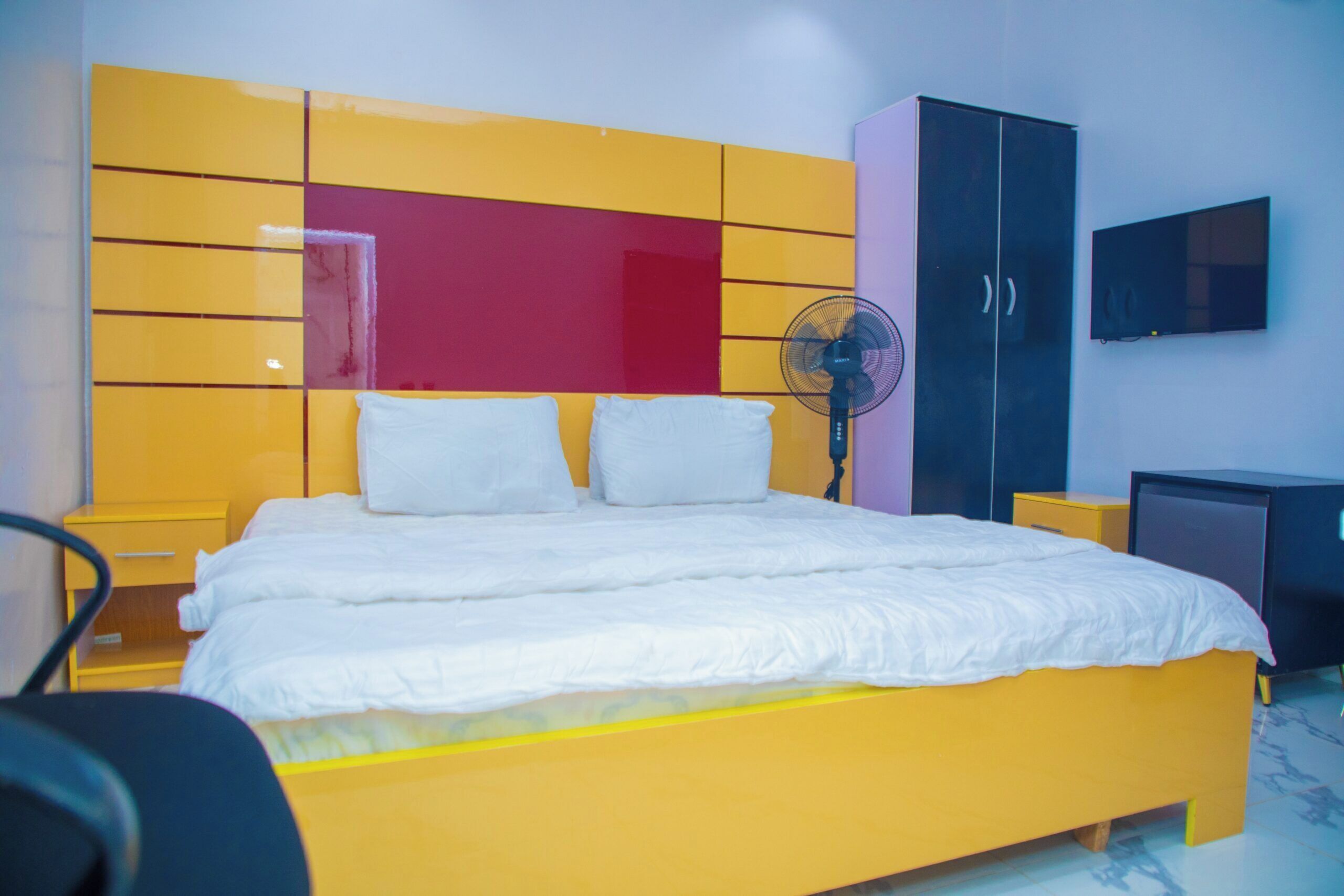 A bed with white bedding, a yellow headboard, and a black cabinet.