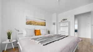 A modern bedroom with a bed, white walls, a painting, a white wardrobe, and a small table with a plant. - Albatros - Sea view, infrared cabin, beach chair, private parking, terrace (Olpenitz)