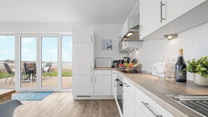 A modern kitchen with white cabinets, a wooden countertop, and a view of the outdoors through large sliding doors. - Albatros - Sea view, infrared cabin, beach chair, private parking, terrace (Olpenitz)