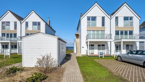 A row of white two-story houses with balconies, a paved walkway, and a car parked in front. - Albatros - Sea view, infrared cabin, beach chair, private parking, terrace (Olpenitz)