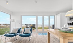 Une cuisine moderne avec une table à manger en bois, un îlot central et une vue sur la mer grâce à de grandes portes coulissantes.