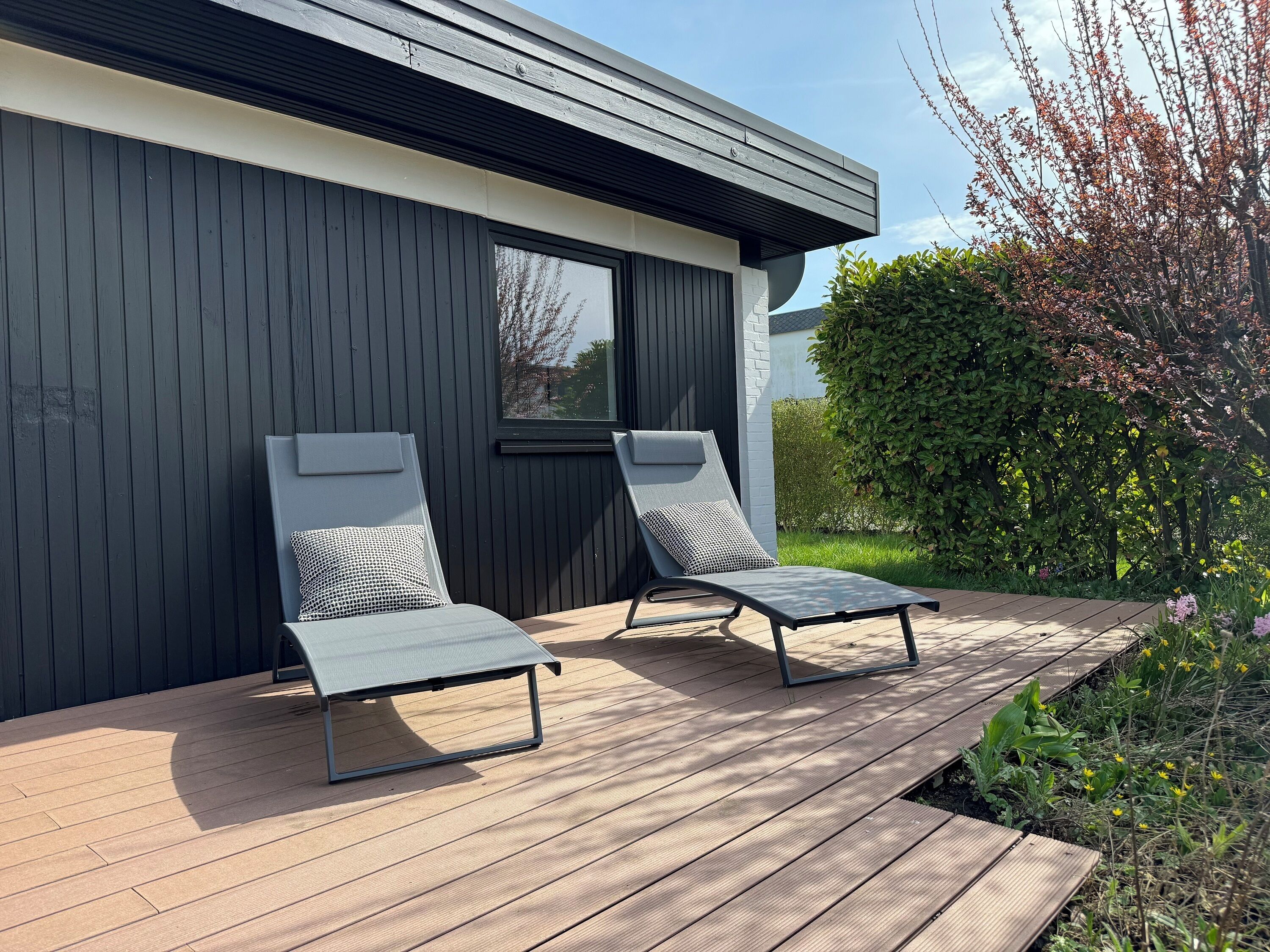Een moderne buitenruimte met twee loungestoelen en een houten terras.