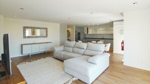Un salon moderne avec un canapé d’angle, un téléviseur à écran plat, une console blanche et un grand miroir.