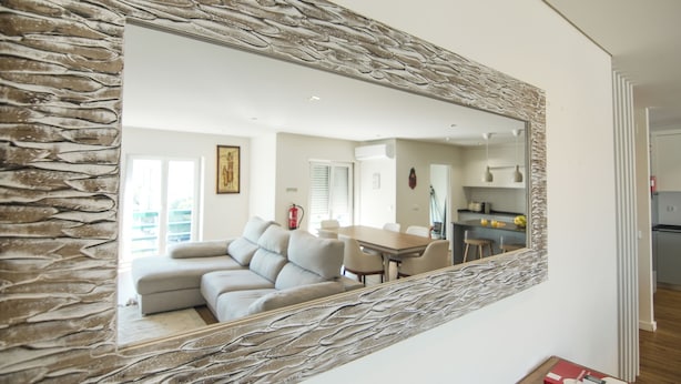 Un salon avec un miroir encadré de pierres, un canapé et, au fond, un coin repas.