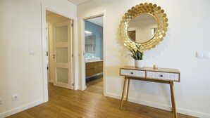 Un couloir au plancher de bois menant à une salle de bain équipée d’un lavabo et d’un miroir.