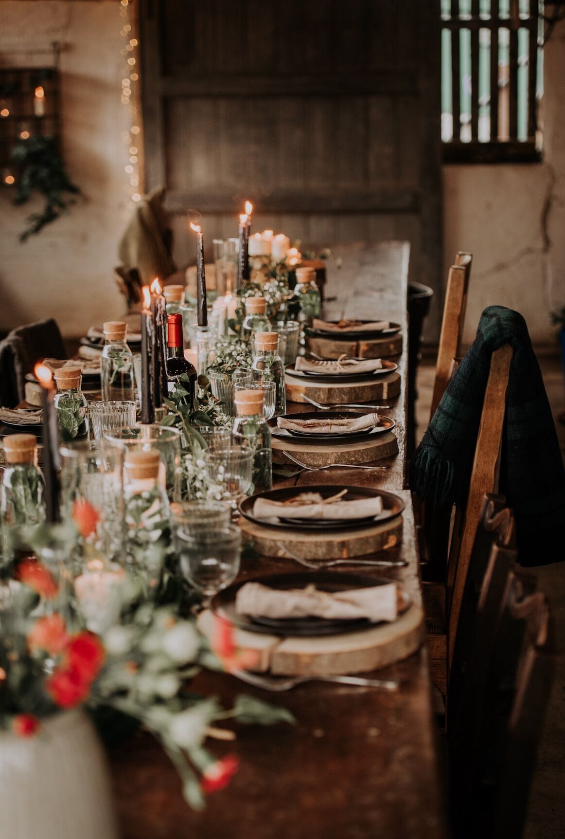 A long dining table set with candles, glass bottles, and plates.