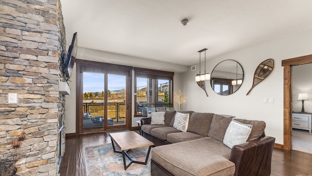 A modern living room with a stone accent wall, a sectional sofa, a coffee table, and a large window offering a view of the outdoors. - 500 ft from Pickleball | Private Gondola Access | Hot Tubs & Fitness Center (Steamboat Springs)