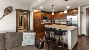 A modern kitchen with wooden cabinets, a large island with bar stools, a microwave, and a refrigerator. - 500 ft from Pickleball | Private Gondola Access | Hot Tubs & Fitness Center (Steamboat Springs)