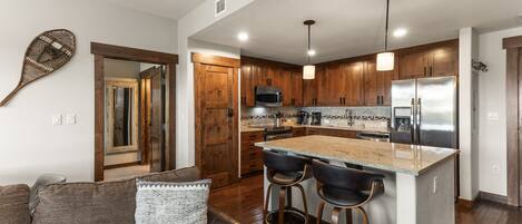 A modern kitchen with wooden cabinets, a large island with bar stools, a microwave, and a refrigerator.